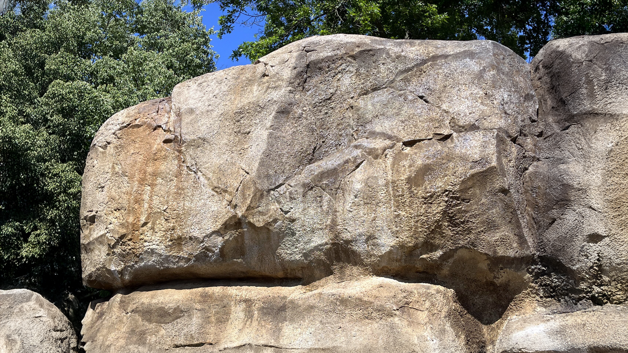 Realistic cast concrete boulder in the foreground with a collection of smaller artificial rock pieces displayed on wooden stairs in the background