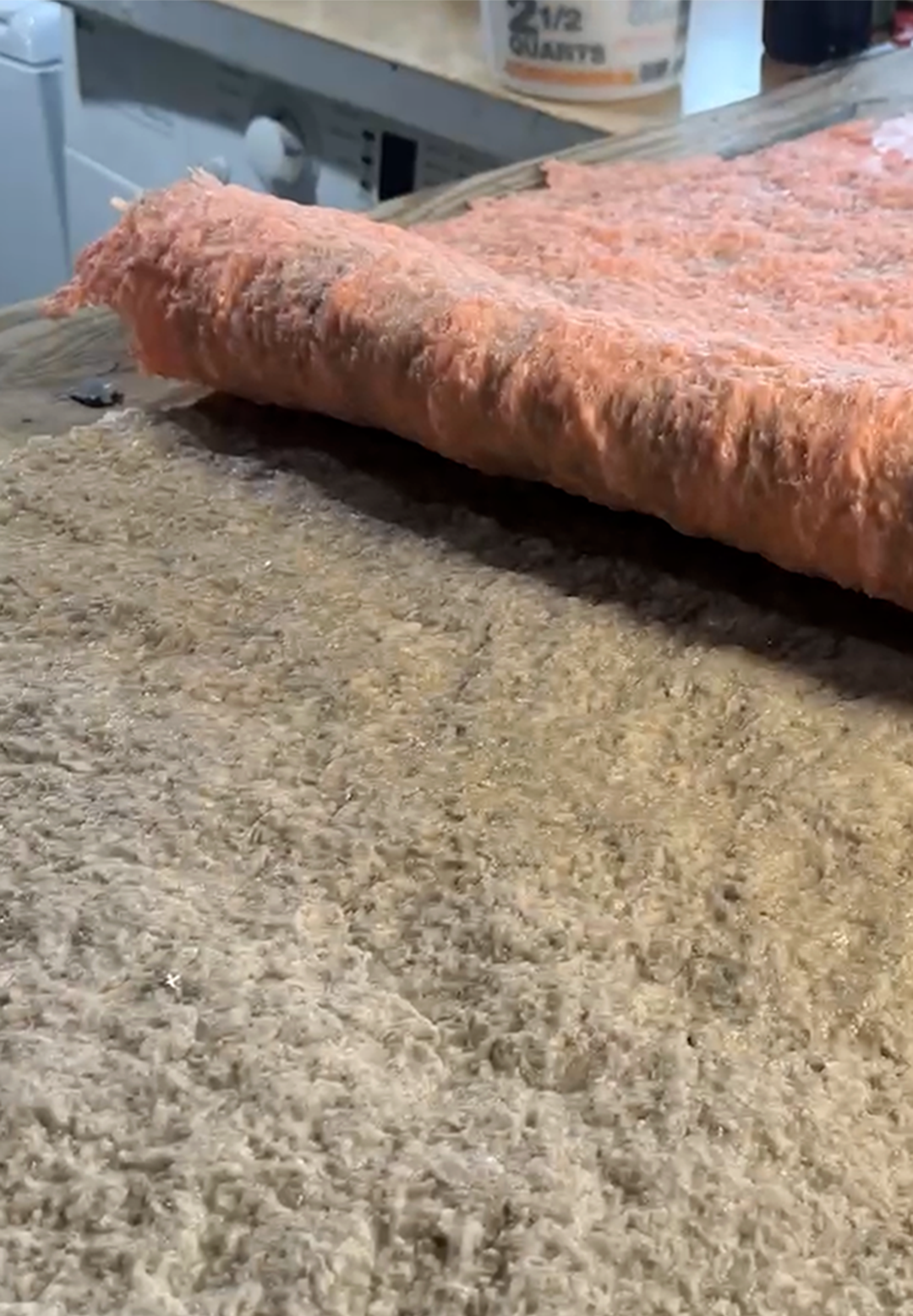 Close-up side view of an orange-coated foam mold material being peeled away from a textured concrete surface, revealing the detailed rock texture underneath
